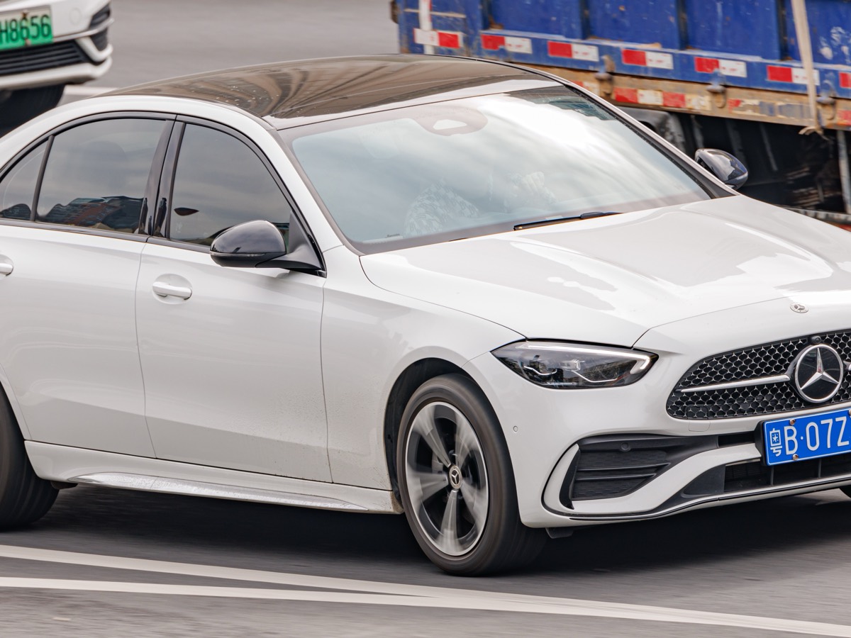 လမ်းပေါ်တွင် မောင်းနှင်နေသော အဖြူရောင် Mercedes-Benz C-Class ဆီဒန်း